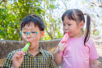 Little asian siblings eating ice cream together in park