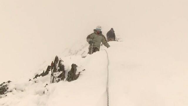 A group of climbers descend from the top in a snow blizzard
