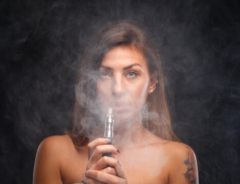 Young beautiful woman smoking ( vaping ) e-cigarette.  A cloud of vapor.