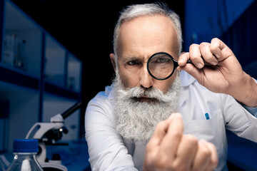 portrait of focused scientist looking at hand through magnifying glass in laboratory