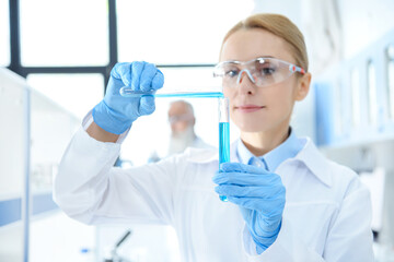 Smiling chemist in white coat holding test tubes with reagents and making experiment