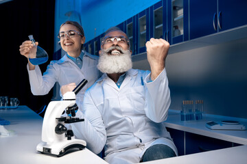 scientist using microscope while colleague holding reagent in tube in lab. scientists working together in laboratory