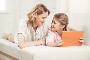 happy mother and daughter using digital tablet while lying on sofa