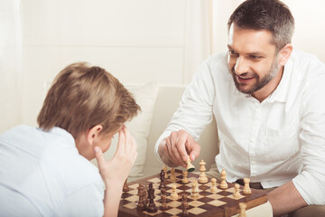 little boy playing chess together with smiling father at home