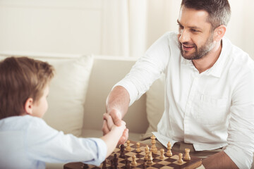 father and son shaking hands after playing chess board game