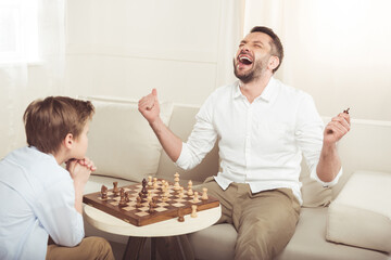man celebrating win in chess game with upset son near by