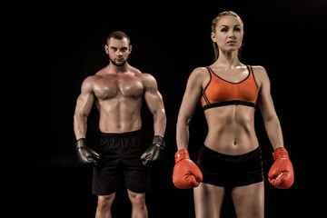 Fototapeta na wymiar Confident muscular young sportsman and sportswoman in boxing gloves standing isolated on black
