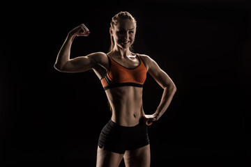 Fototapeta na wymiar young smiling sportswoman flexing biceps and looking at camera