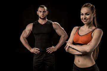 sportive woman looking at camera with man behind isolated on black