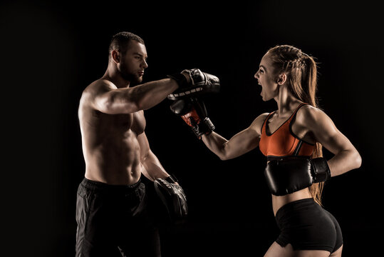 Sporty muscular young man and woman boxing together isolated on black