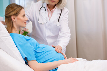 doctor touching belly of pregnant woman lying in hospital bed