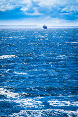 Blue Rough Sea and Freight Ship / Distant cargo vessel at sea horizon with dramatic sky and waves...