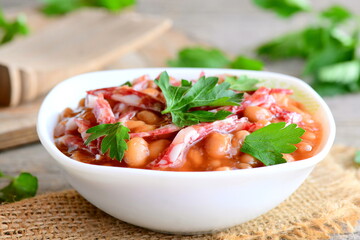Easy white bean stew with smoked sausage, tomato sauce and fresh parsley in a bowl and on a wooden vintage table. Simple slow cooker white bean and smoked sausage. Homemade stew recipe. Closeup
