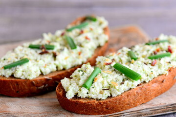 Guacamole toast on a wooden board and vintage table. Homemade toast with sauce guacamole, fresh green onion and dried herbs. Healthy breakfast idea with guacamole on toast. Closeup