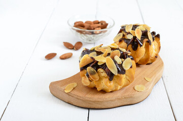 Eclairs, covered with dark chocolate and almond flakes decoration on a white wooden background.