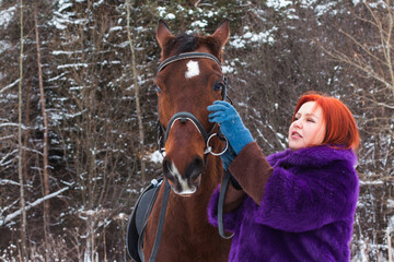 Fototapeta premium Woman with red hair and big horse outdoor in winter