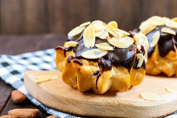 Eclairs, covered with dark chocolate and decoration almond flakes on a dark wooden background.