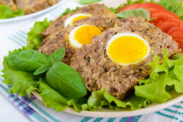 Meatloaf stuffed boiled egg with fresh tomato and lettuce leaves on a plate on a white wooden table.