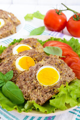 Meatloaf stuffed boiled egg with fresh tomato and lettuce leaves on a plate on a white wooden table.