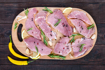 Raw flat meat for steak (chop) with spices on a cutting board on a dark wooden table. Top view.