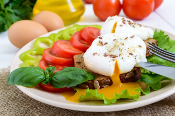 Fototapeta na wymiar Sandwich with egg poached, lettuce, black bread with seeds, tomatoes, sweet pepper on a plate on a white wooden table.