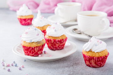 Mini cupcakes with white frosting cream and pink sprinkles on light gray background. Birthday party food concept.