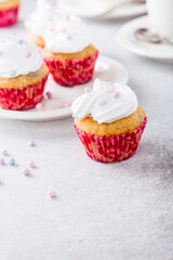 Vanilla cupcakes with white frosting cream and pink sprinkles on light gray background. Birthday party food concept. Copy space.