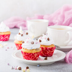 Mini cupcakes with white frosting cream and pink sprinkles on light gray background. Birthday party food concept.