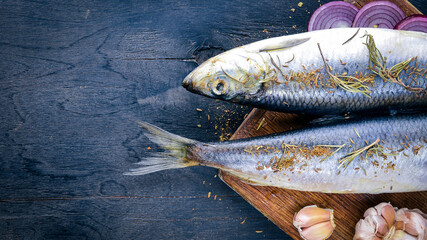 Fresh fish with vegetables, spices and oil. On a black wooden background. Free space for text . Top view