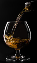 brandy or whiskey pouring into glass on a black background