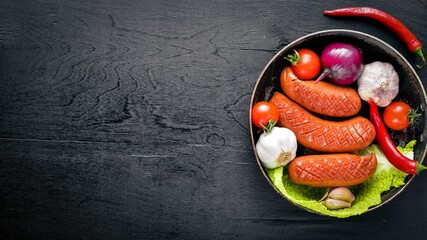 Grilled sausages in a pan with fresh vegetables. Wooden surface. Top view.