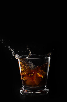 A glass of whiskey and ice cube on a black background