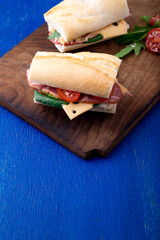 Sandwich with jamon, arugula, tomatoes, cheese on wooden board blue background. Rustic. Two.