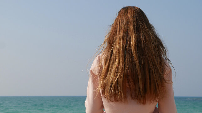 Girl with long ginger red hair enjoying seascape. Sea breeze playing with hair.