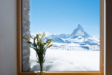Scenic view on snowy Matterhorn peak in sunny day with blue sky and blur window in foreground, Switzerland.