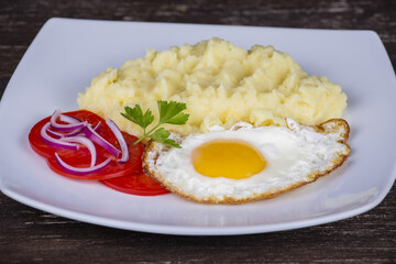 Mashed potatoes with fried eggs and tomato.