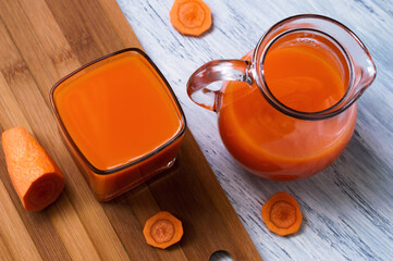 Fresh carrot juice in a glass and a glass jug with bits of carrot