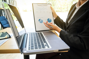 Images of businesswoman showing and presenting for financial graph on clipboard with computer labtop on her wooden desk in office