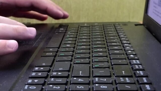 Caucasian man hands printing on laptop keyboard. Closeup view of computer with green wall behind. Office scene.