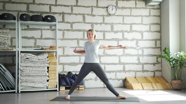 Mature woman practices yoga and does asanas using sports equipment. Woman of 30-35 years of age does gymnastics, uses sports equipment and makes leans to the left, right, straight.