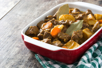 Beef meat stewed with potatoes, carrots and spices in ceramic pot on wooden table
