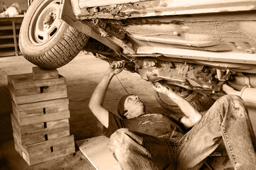 A worker is repairing an old car. Black and white.