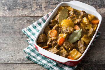 Beef meat stewed with potatoes, carrots and spices in ceramic pot on wooden table
