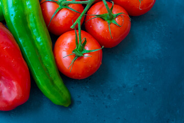 Fresh organic vegetables, tomatoes on a vine, green italian and red bell peppers, dark blue background, styled image, top view