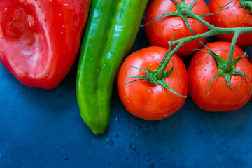 Fresh organic vegetables, tomatoes on a vine, green italian and red bell peppers, water drops, dark blue background, styled image