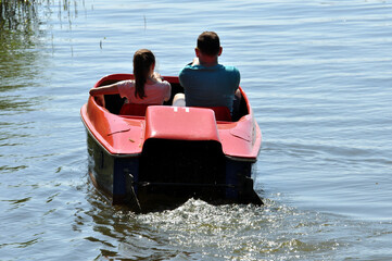 Ein rotes Tretboot mit zwei Personen fahren auf den See, hinaus, im Gegenlicht