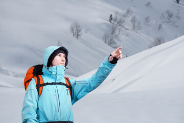 The mountaineer pointing at peak, standing against a winter mountain landscape.