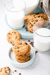 Stack of chocolate chip cookies on blue stone plate with glass of milk on light gray background. Selective focus.