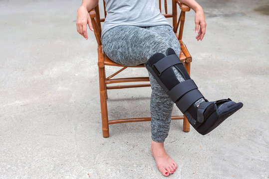 injury woman with black cast on leg  sitting on wooden chair at home, Travel insurance concept
