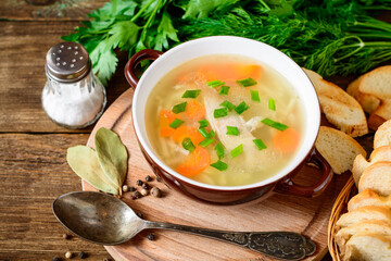 Homemade chicken soup with noodles and vegetables in ceramic bowl on wooden table.